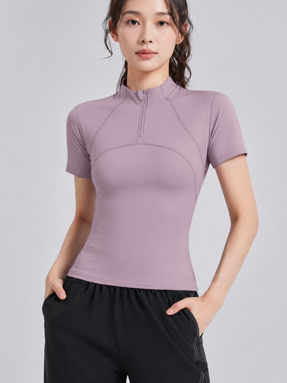 Woman wearing a purple athletic top and black pants on a light gray background