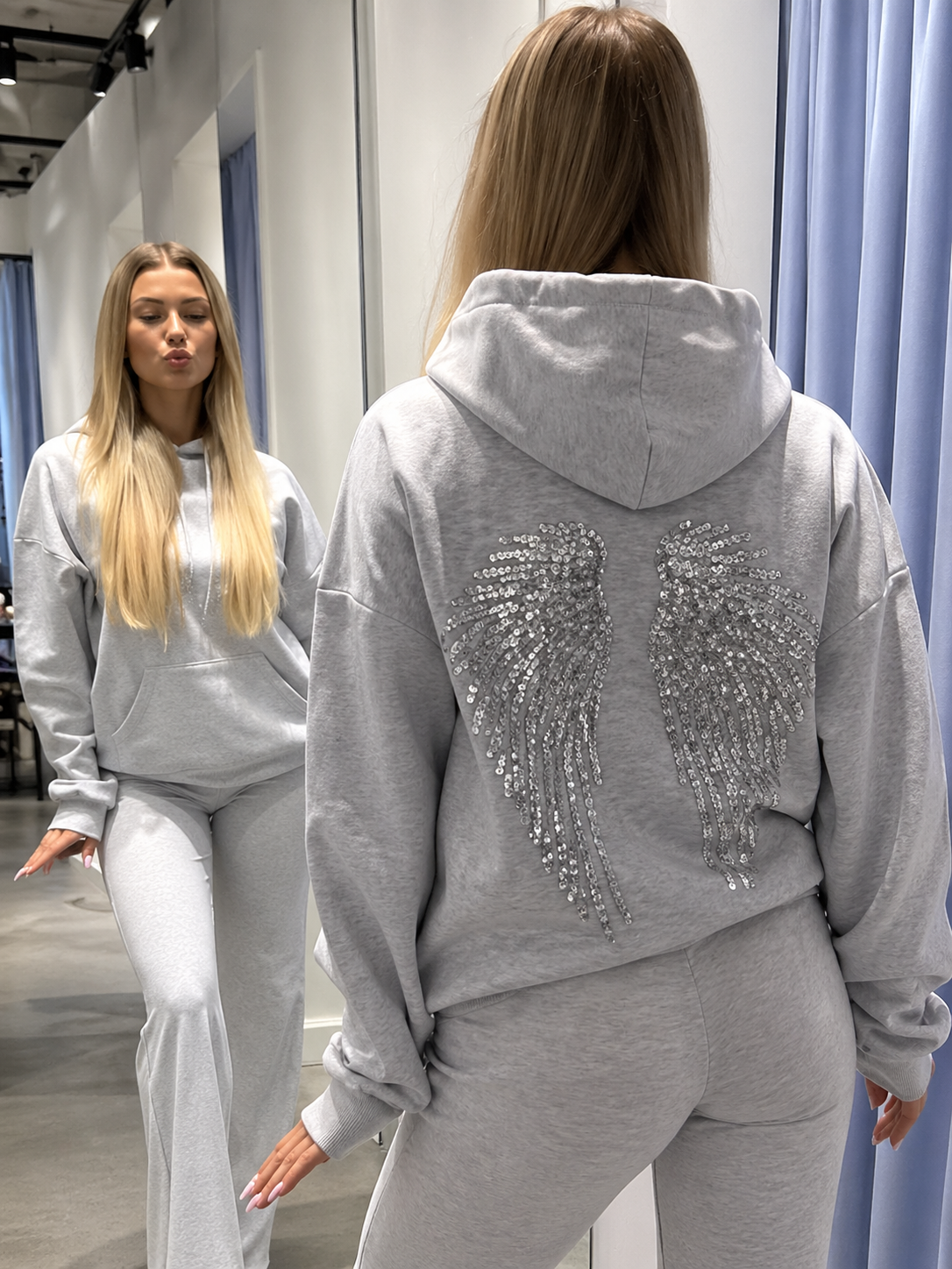 Woman wearing a gray hoodie with angel wings design in a store setting
