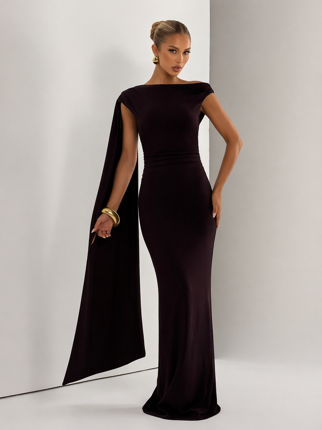 Woman wearing a black evening gown with a cape against a white background