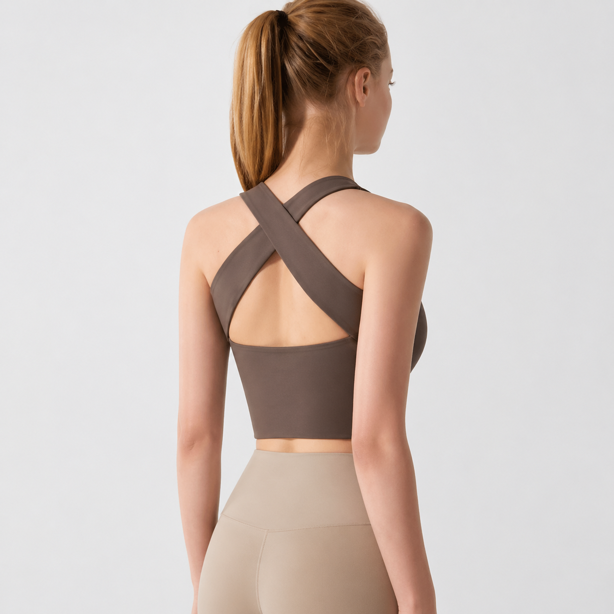 Woman wearing a brown sports bra with criss-cross straps on a light gray background