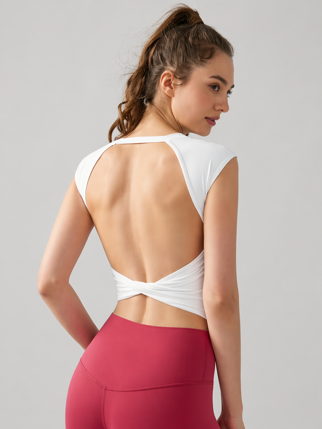 Woman wearing a white open-back top and pink leggings on a gray background