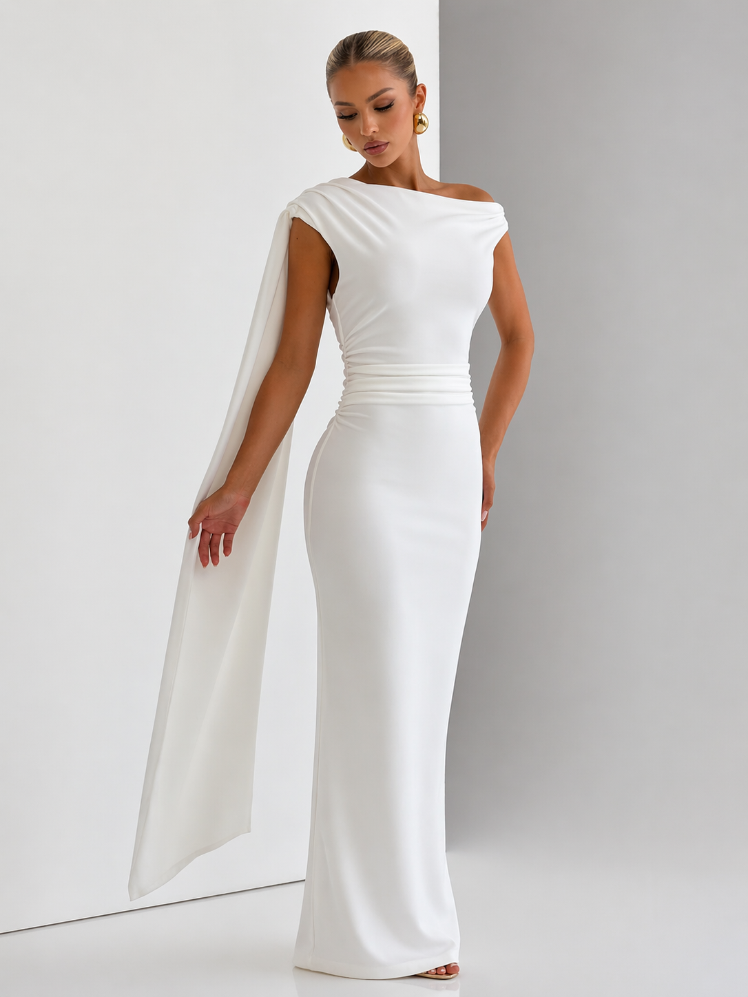 Woman wearing a white gown with a cape against a plain background