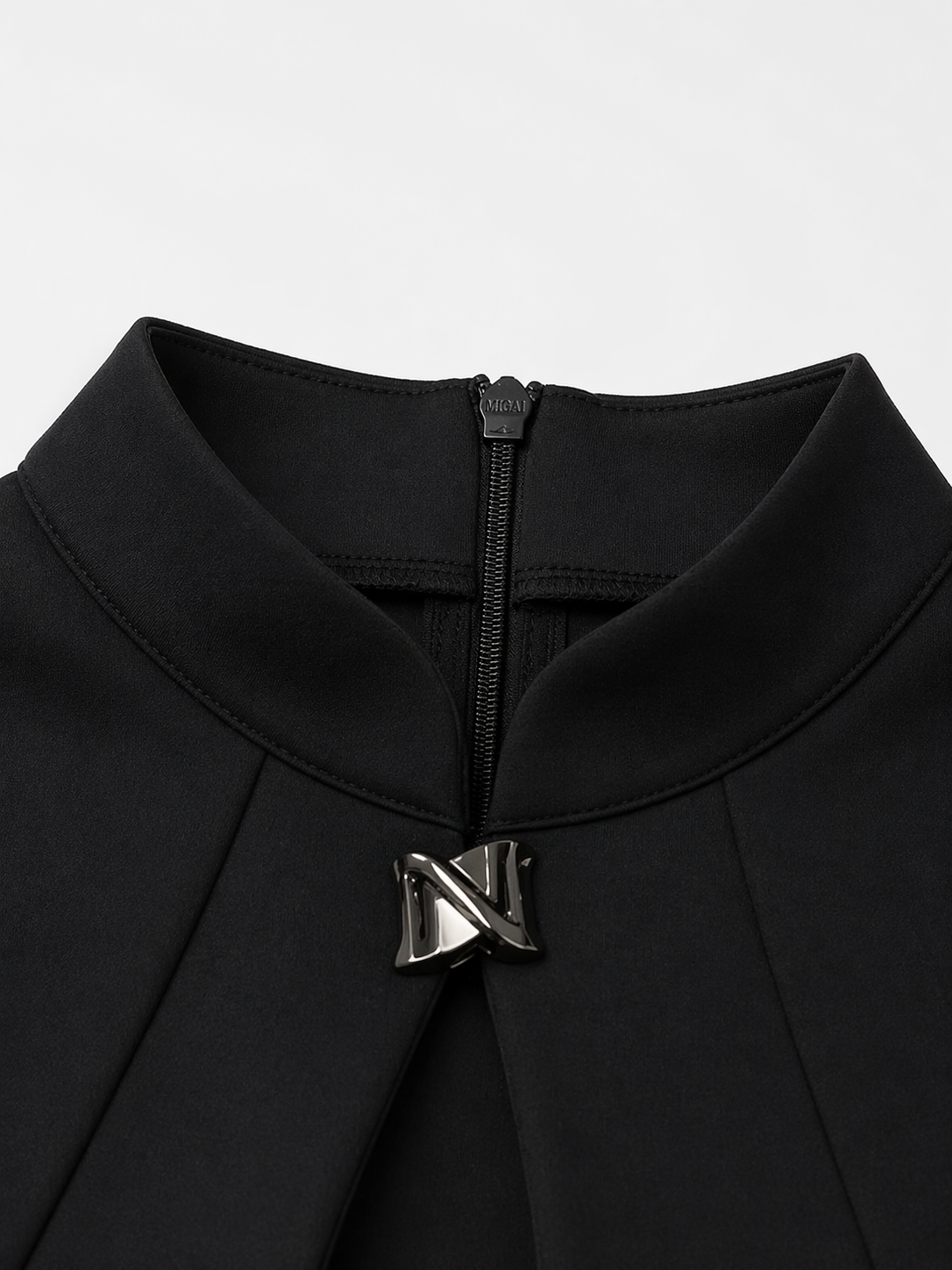 Close-up of a black garment with a zipper and logo on a light gray background