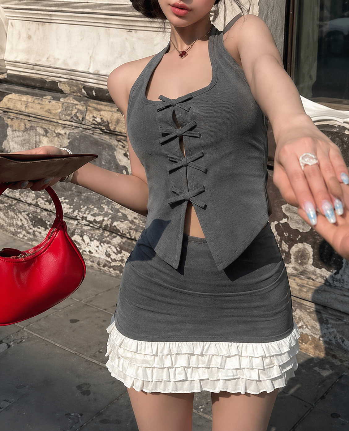 Woman in gray halter top and white skirt holding a red handbag on a street.