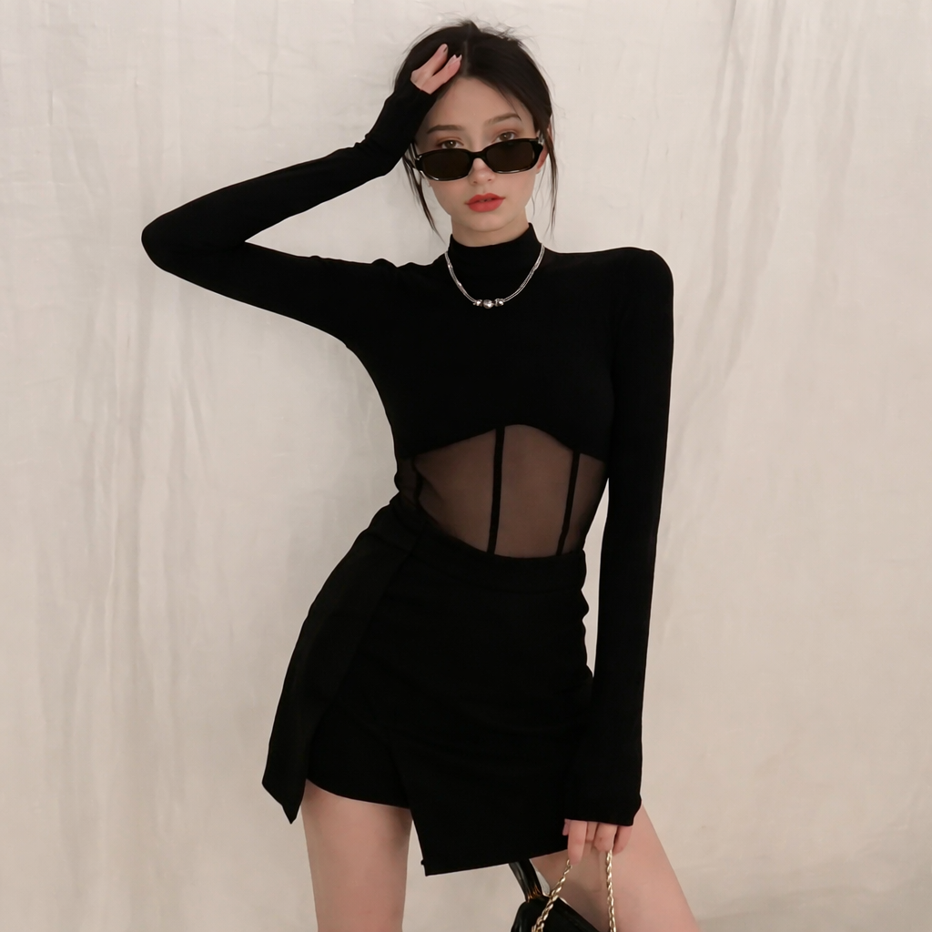 Person wearing a black long-sleeve top with sheer details and a black skirt against a plain background