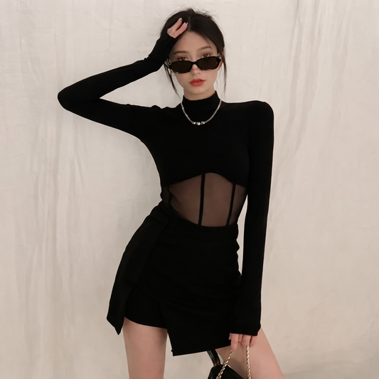 Person wearing a black long-sleeve top with sheer details and a black skirt against a plain background