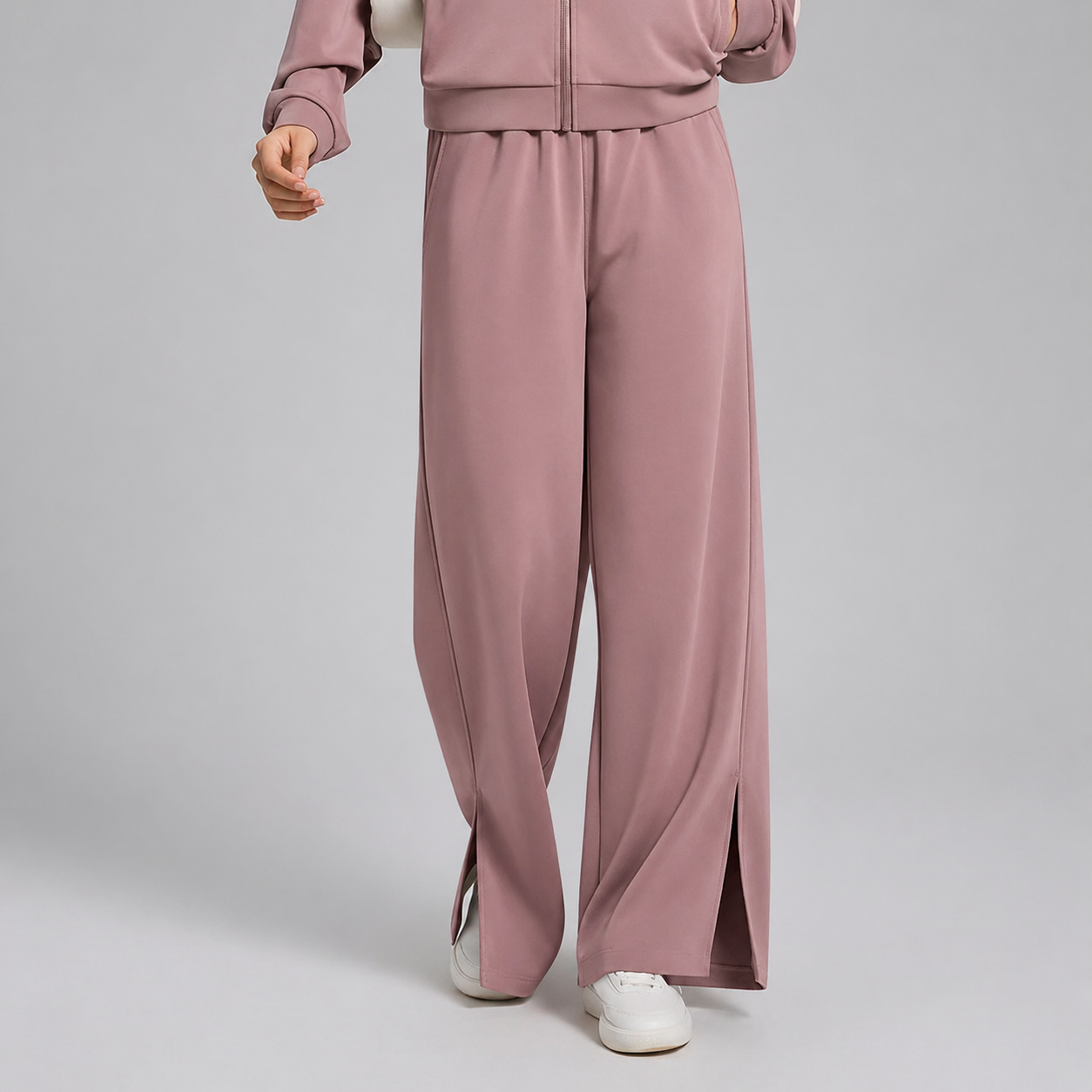 Person wearing a pink tracksuit with wide-leg pants on a light gray background