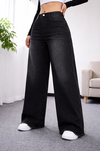 Person wearing black wide-leg jeans in a room with a plant and sofa.