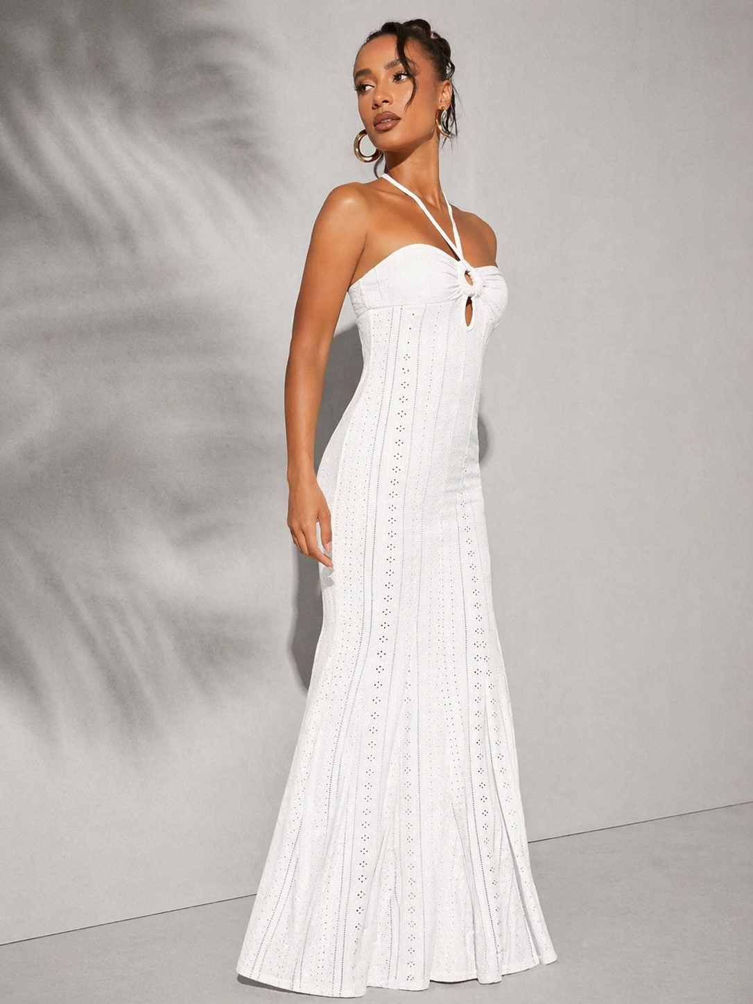 Woman wearing a white strapless dress with cut-out details against a gray background
