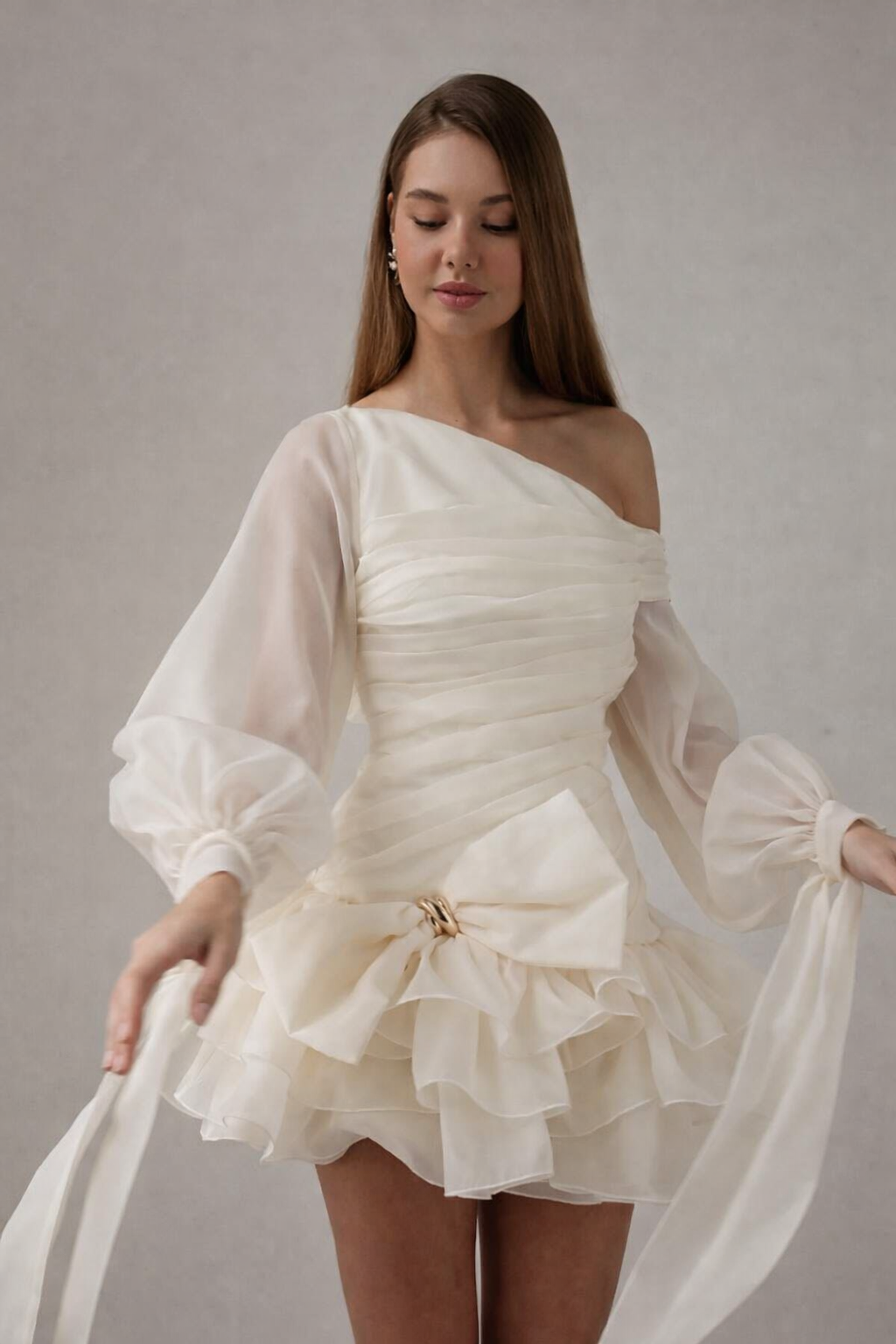Woman wearing a white off-shoulder dress with ruffles and a bow on a plain background