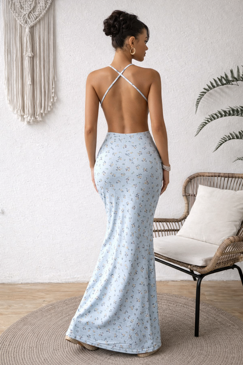 Woman wearing a light blue floral dress with thin straps in a room with a chair and decorative wall hanging.