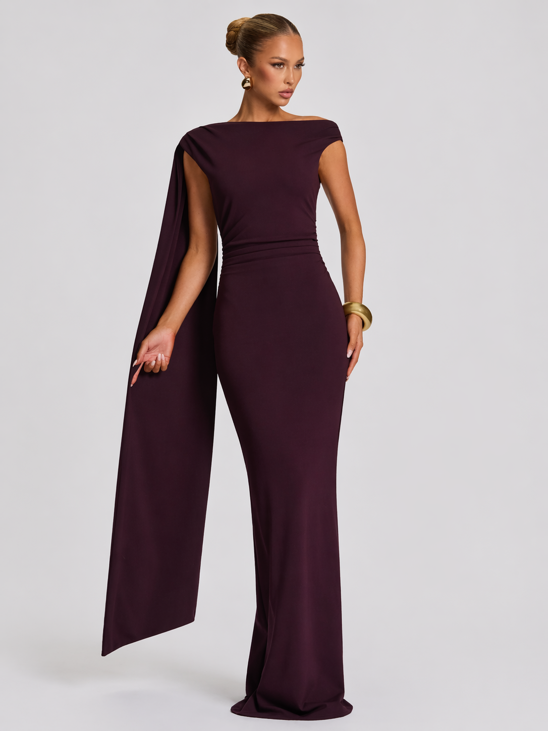 Woman wearing a burgundy jumpsuit with a cape on a white background