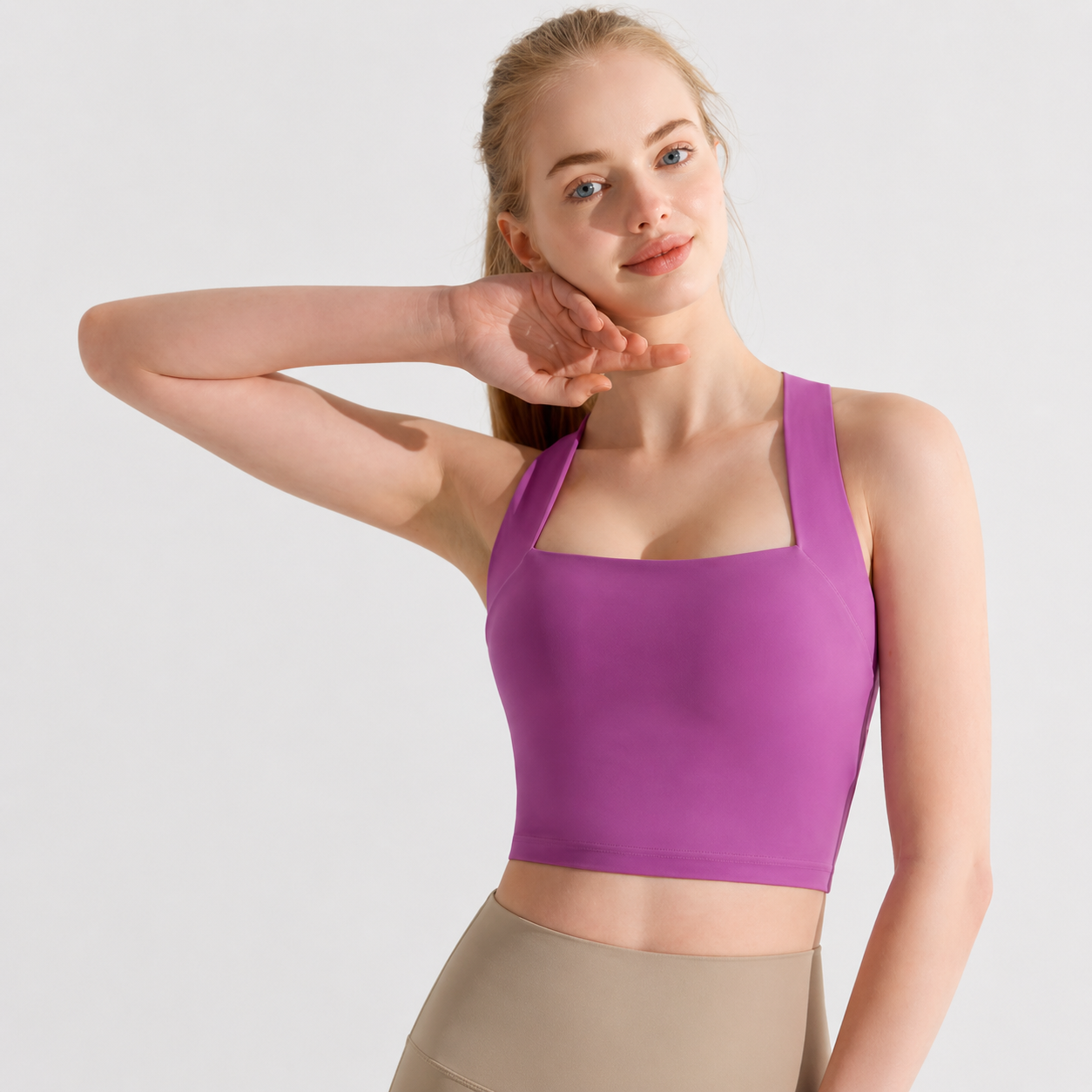 Woman wearing a purple sports bra and beige pants on a light gray background