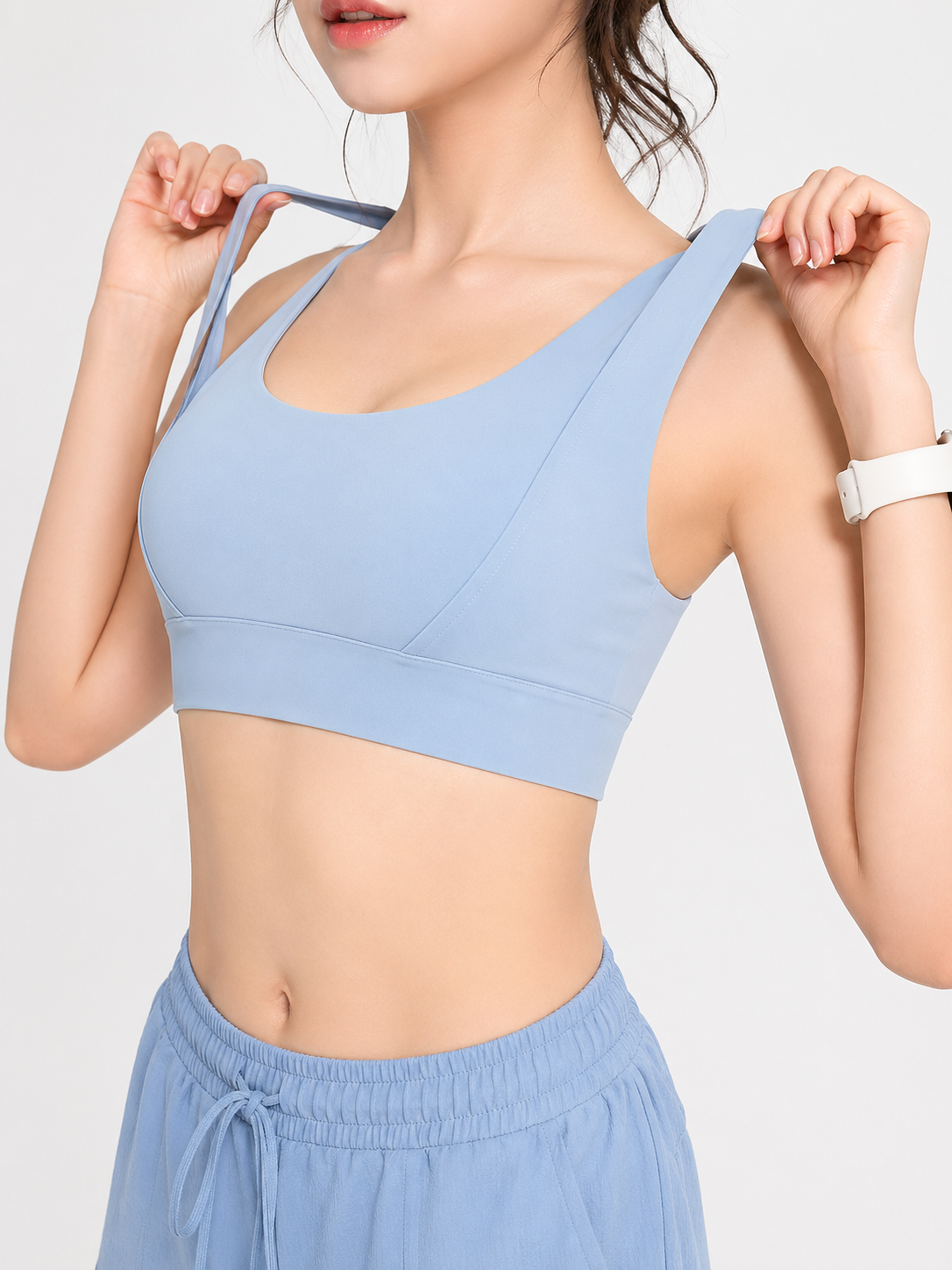 Woman wearing a light blue sports bra and shorts on a plain background