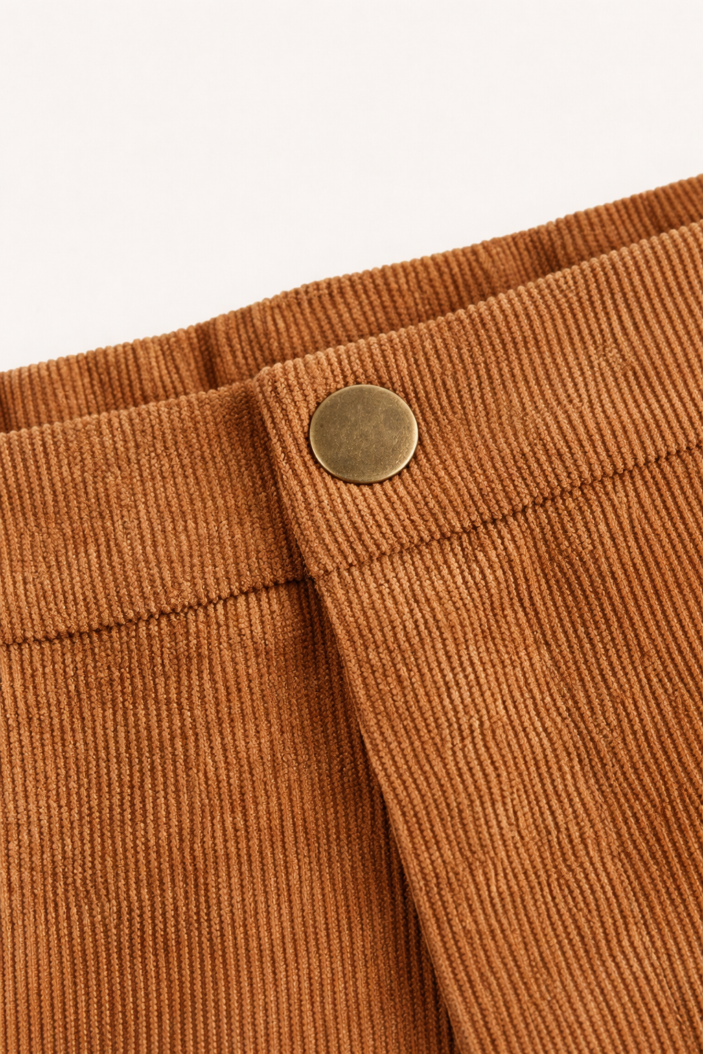 Close-up of brown corduroy pants with a button on a white background