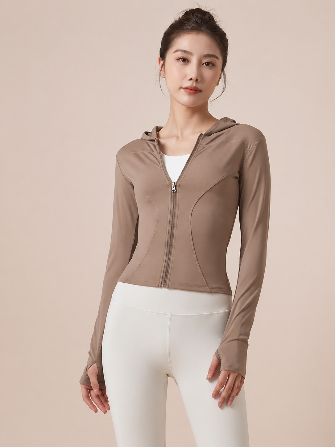 Woman wearing a brown zip-up hoodie and white pants on a beige background