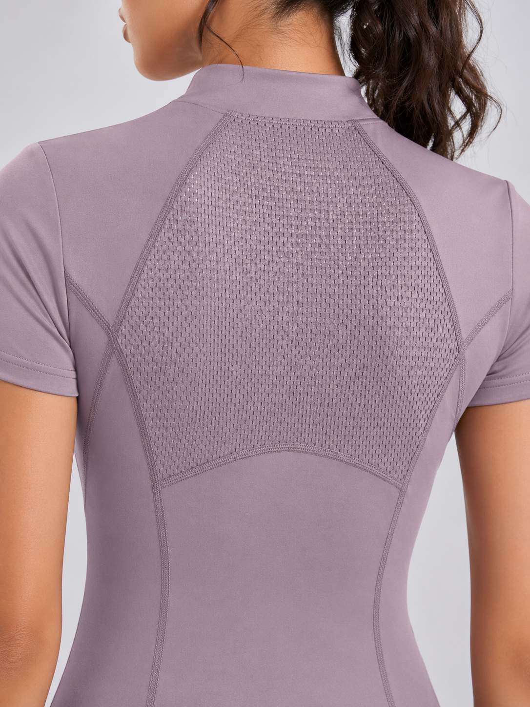 Close-up of a person wearing a mauve athletic top with mesh back on a light gray background