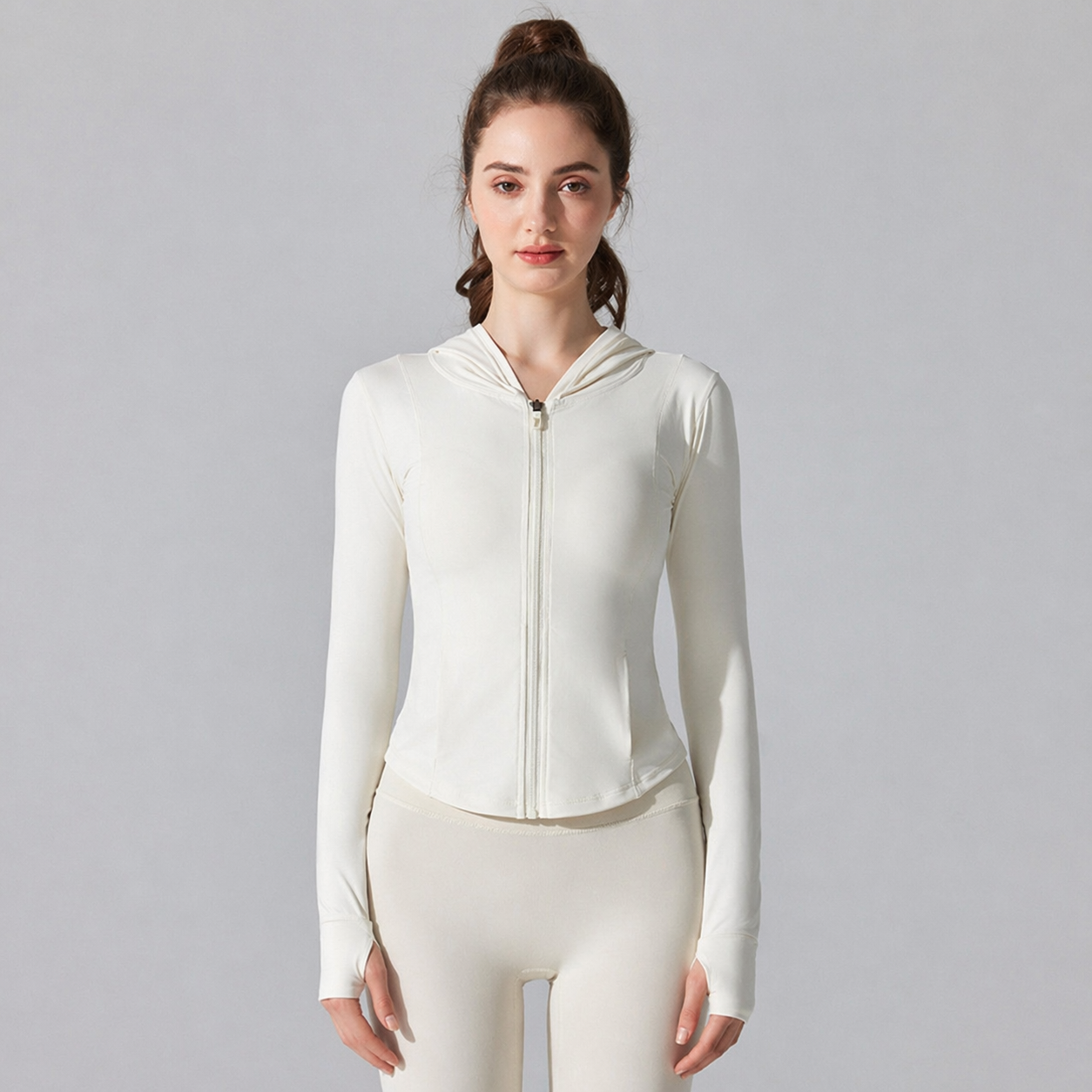 Woman wearing a white zip-up hoodie and leggings on a gray background