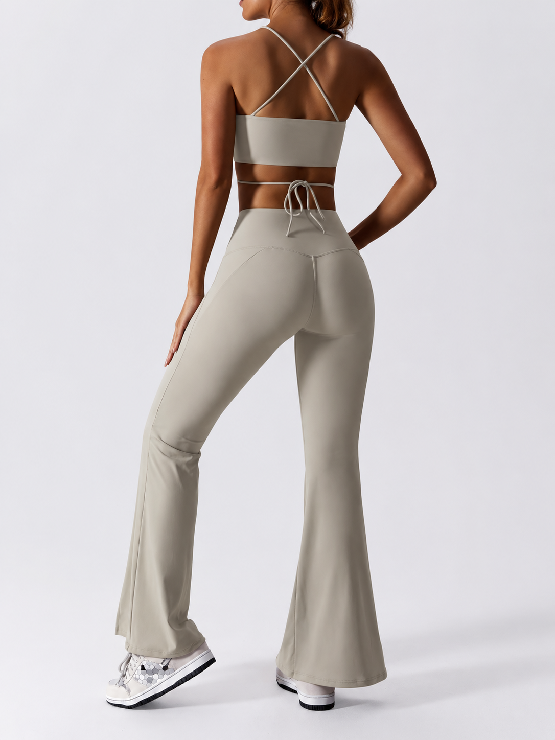 Person wearing a beige sports bra and flared pants on a white background