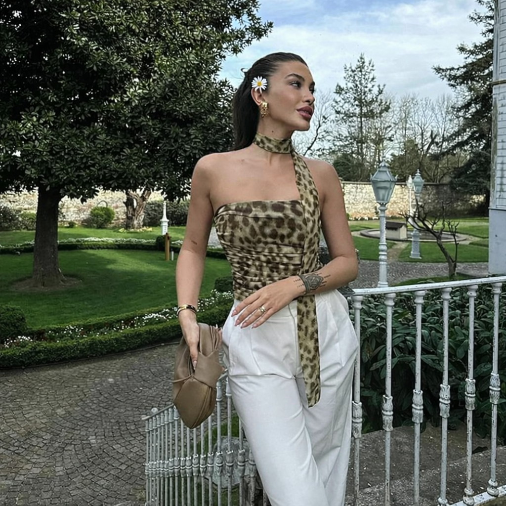 Woman in leopard print top and white pants standing in a garden.