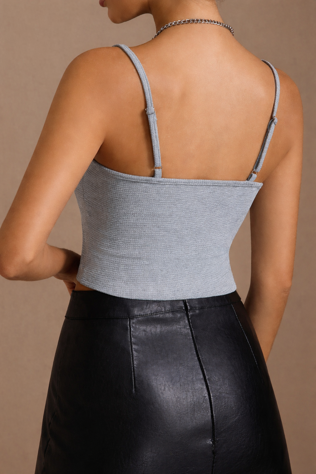 Person wearing a gray crop top and black leather skirt on a beige background