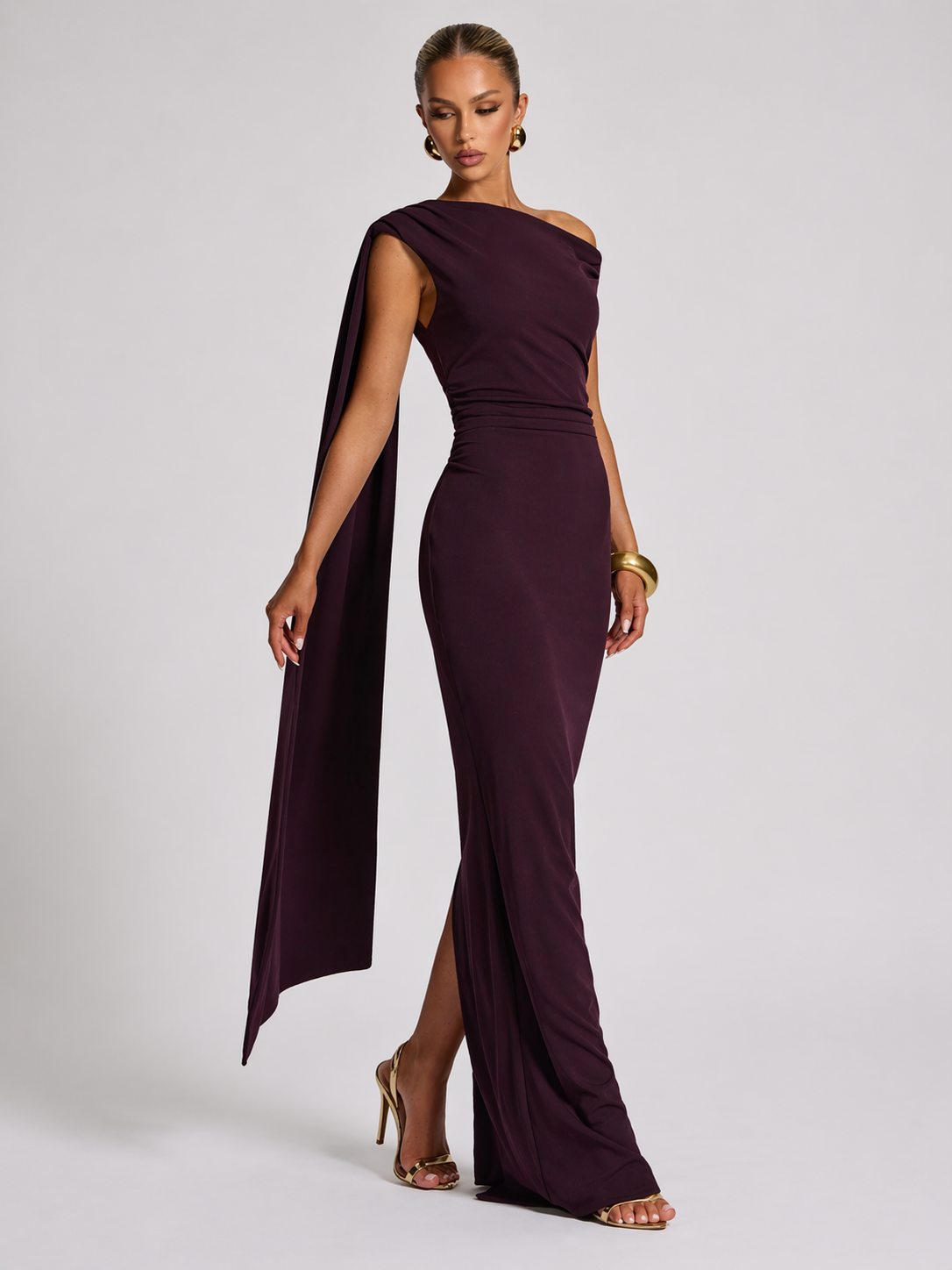 Woman wearing a burgundy one-shoulder gown with a slit on a white background