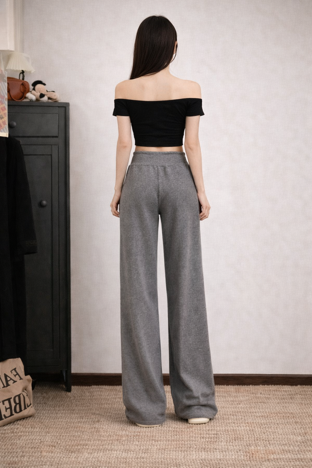 Woman wearing a black off-shoulder top and gray wide-leg pants in a room.