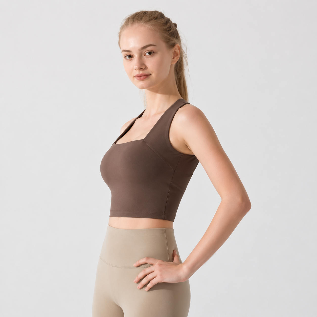 Woman wearing a brown sports bra and beige leggings on a light gray background