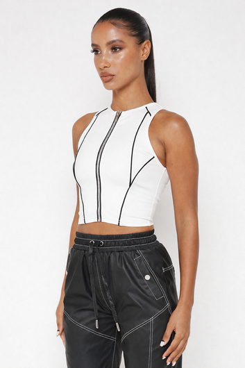 Woman wearing a white sleeveless top with black zipper details and black pants on a white background