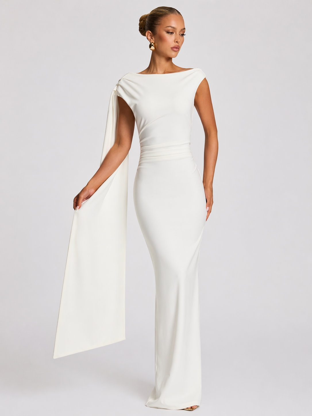 Woman wearing a white gown with a cape on a plain background