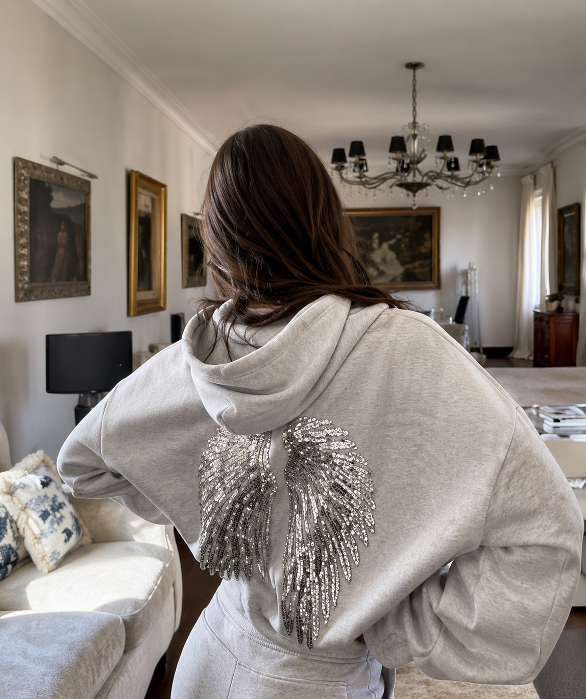 Person wearing a light gray hoodie with decorative elements in a living room setting