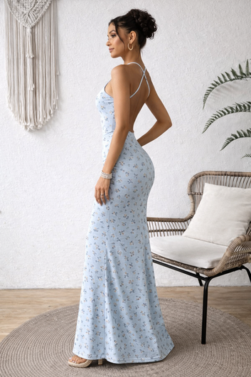 Woman in a light blue floral dress standing in a room with a chair and decorative wall.