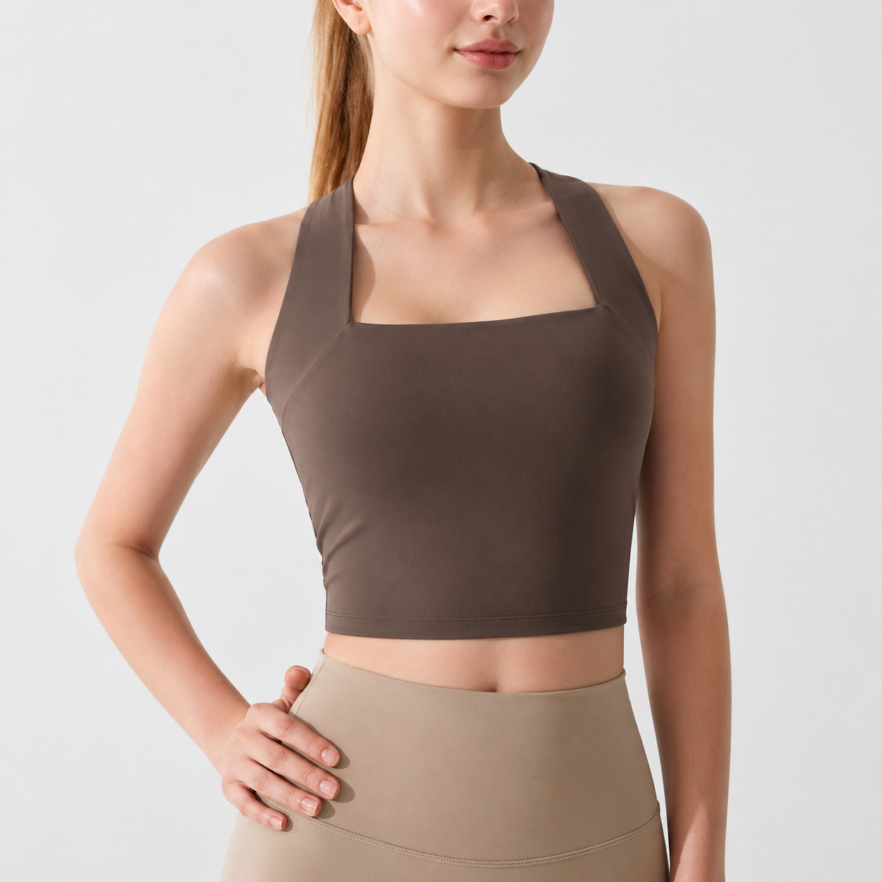 Woman wearing a brown sports bra and beige leggings on a light gray background