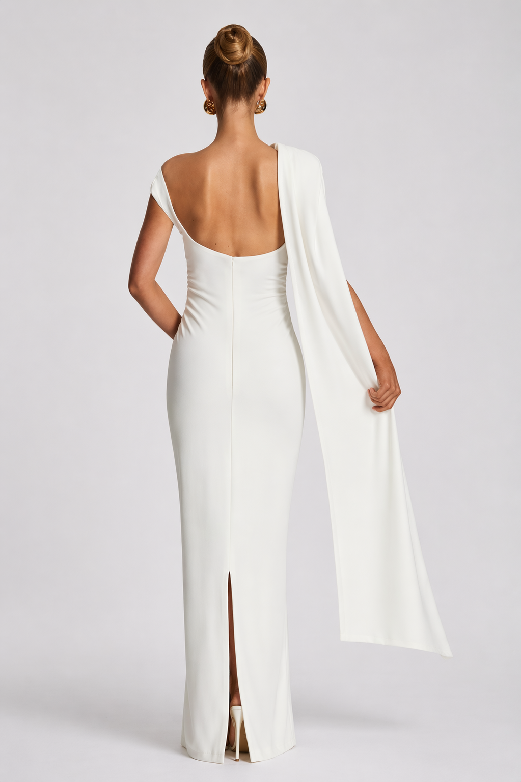 Woman wearing a white evening gown with a cape on a plain background
