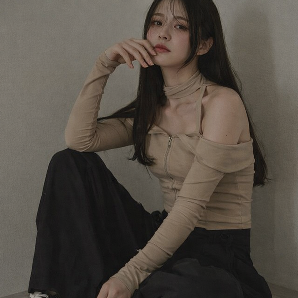 Woman wearing a beige long-sleeve top and black pants against a plain background
