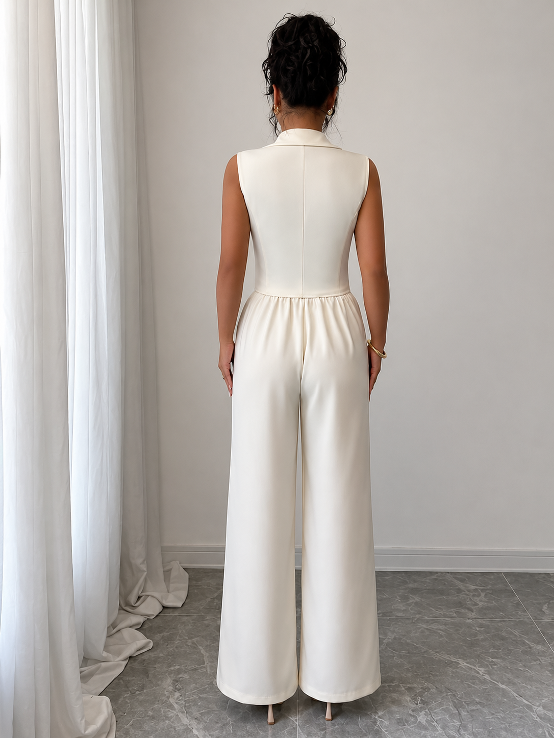 Woman wearing a white sleeveless jumpsuit standing in a room with light gray walls and a gray floor.
