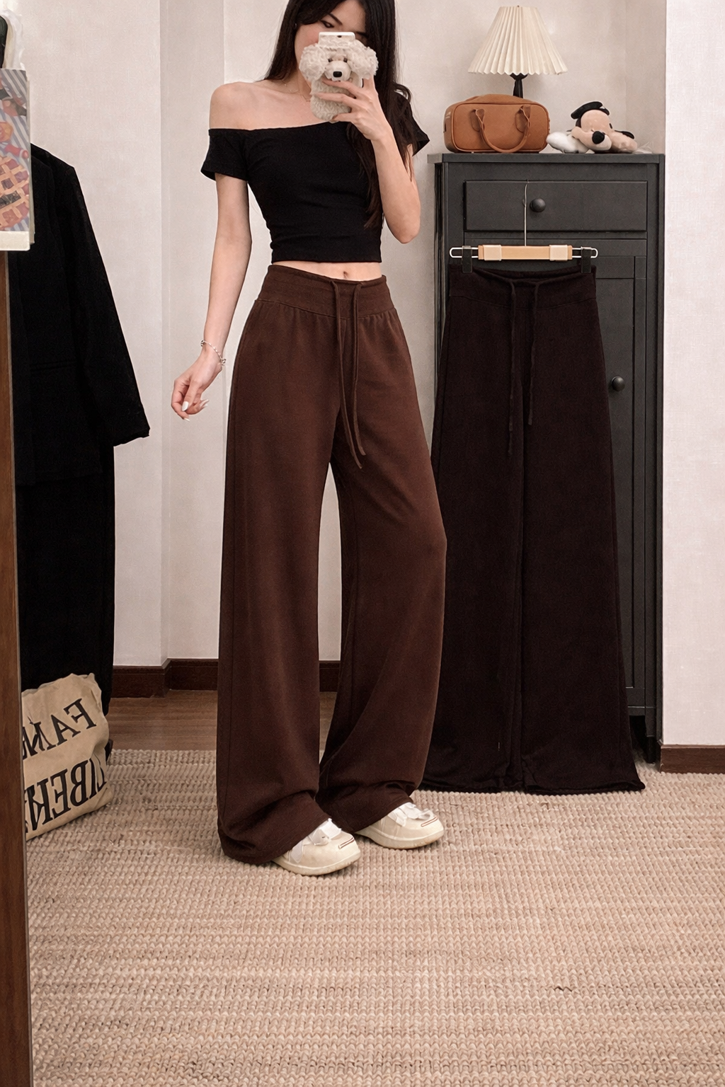 Person wearing a black off-shoulder top and brown wide-leg pants in a room.