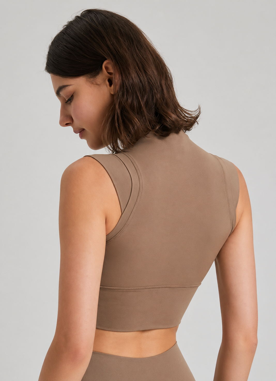 Woman wearing a brown sleeveless top against a plain background