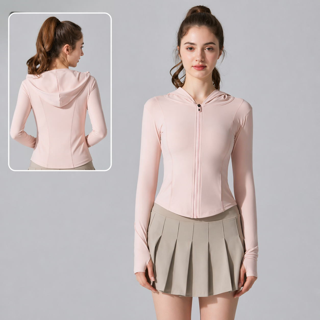 Woman wearing a light pink zip-up hoodie and beige pleated skirt on a gray background