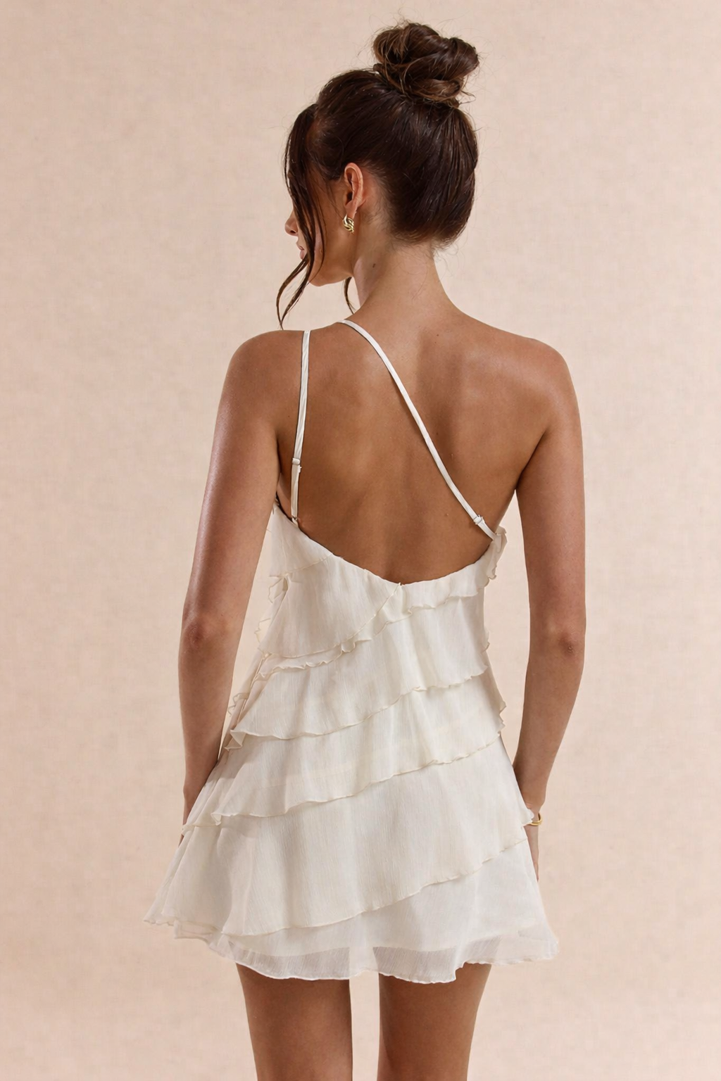 Woman wearing a white ruffled dress with thin straps on a beige background