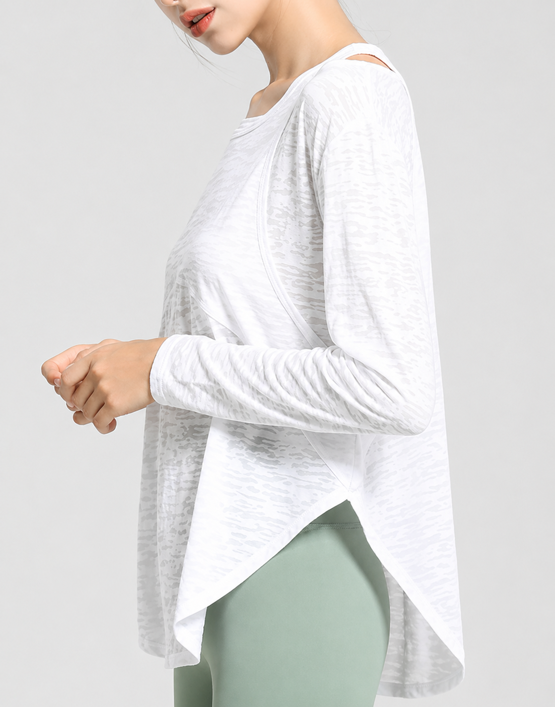 Woman wearing a white long-sleeve top and light green leggings on a plain background