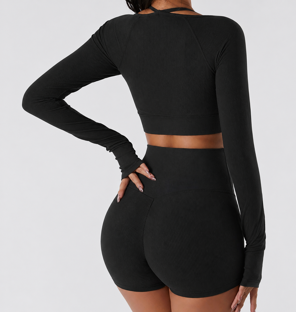Person wearing a black long-sleeve crop top and high-waisted leggings on a light gray background