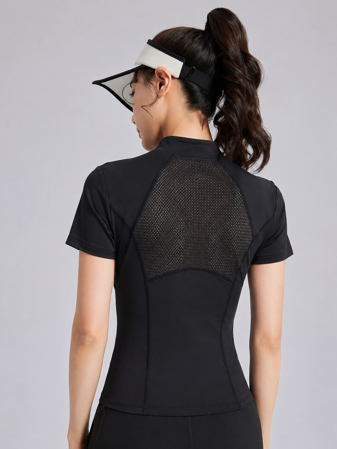 Person wearing a black athletic outfit with mesh back on a gray background