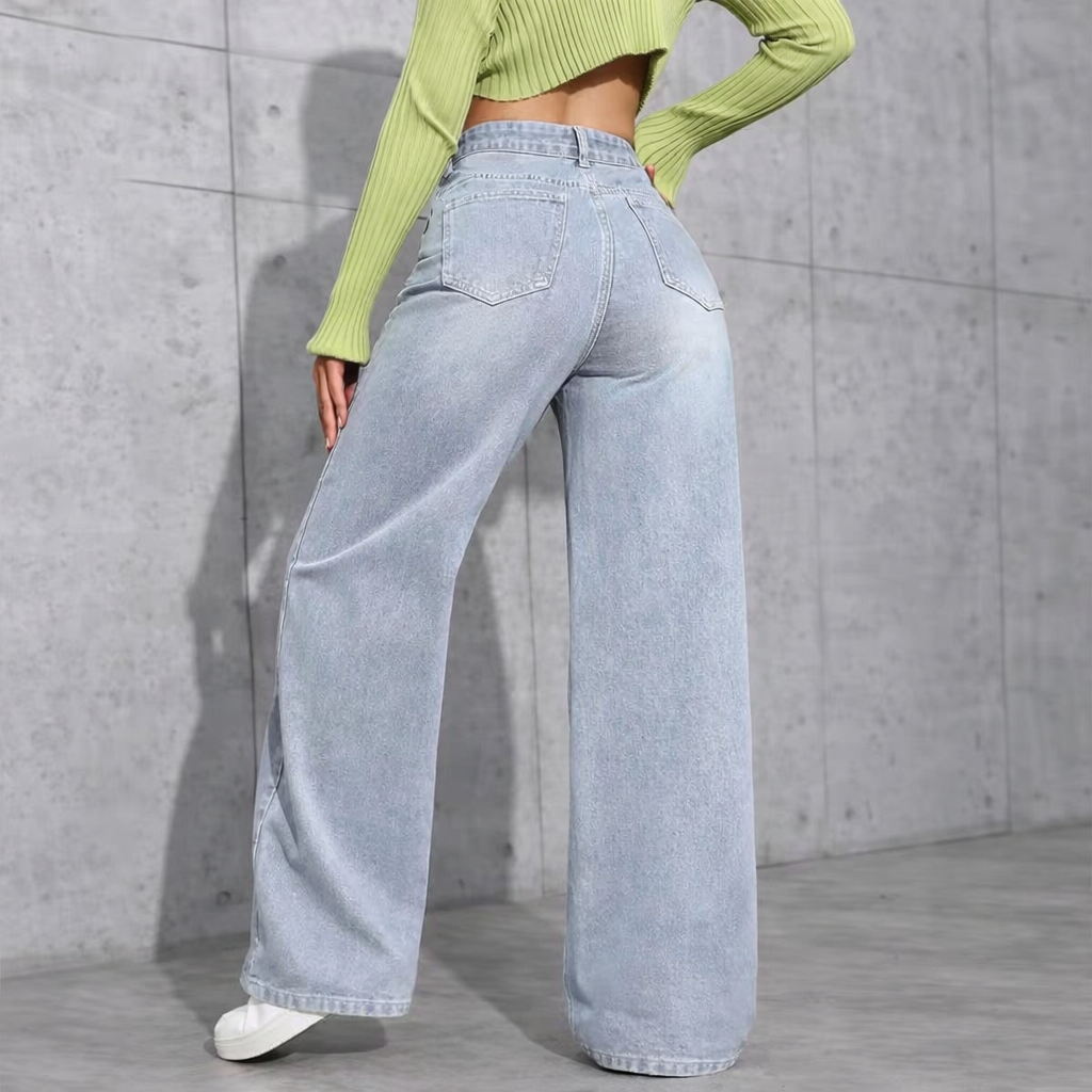 Person wearing light blue jeans and a green cropped top against a gray concrete wall.