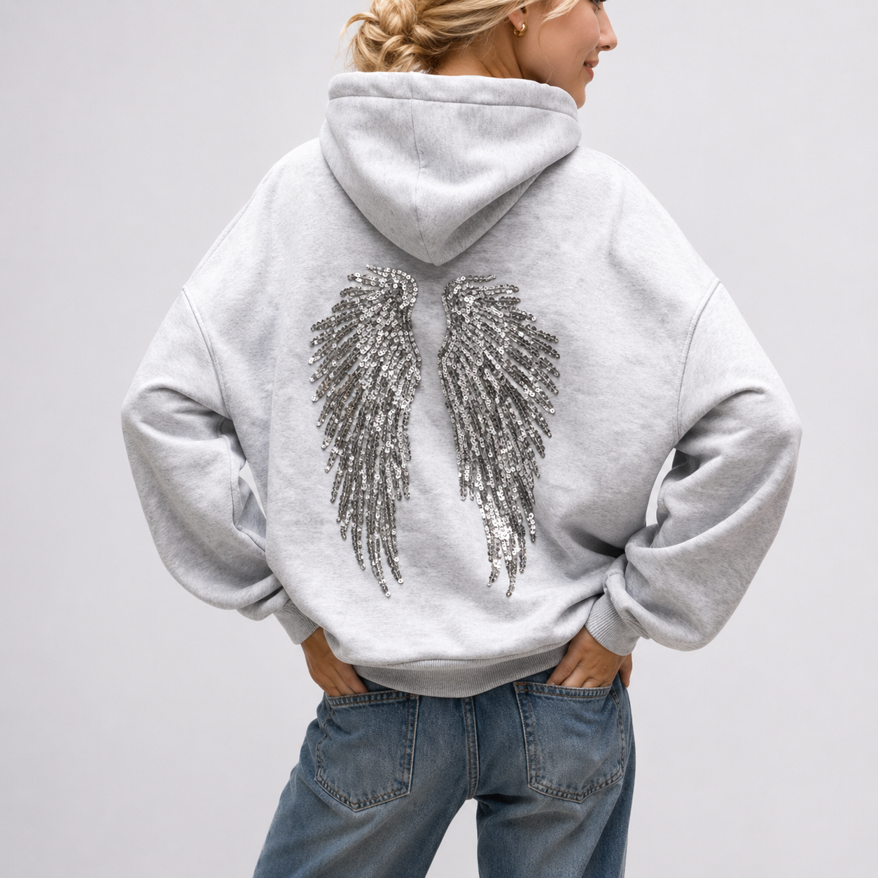 Gray hoodie with sequin wings on the back worn by a person against a plain background