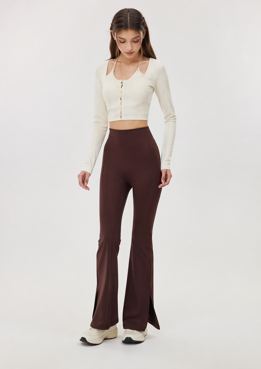 Woman wearing a white long-sleeve top and brown flared pants on a white background