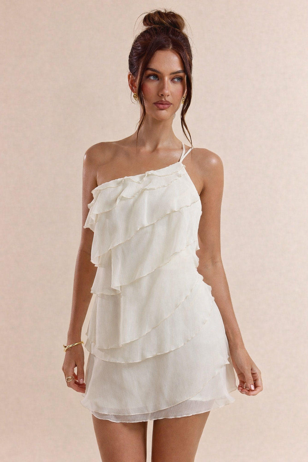 Woman wearing a white one-shoulder dress with ruffled layers on a beige background