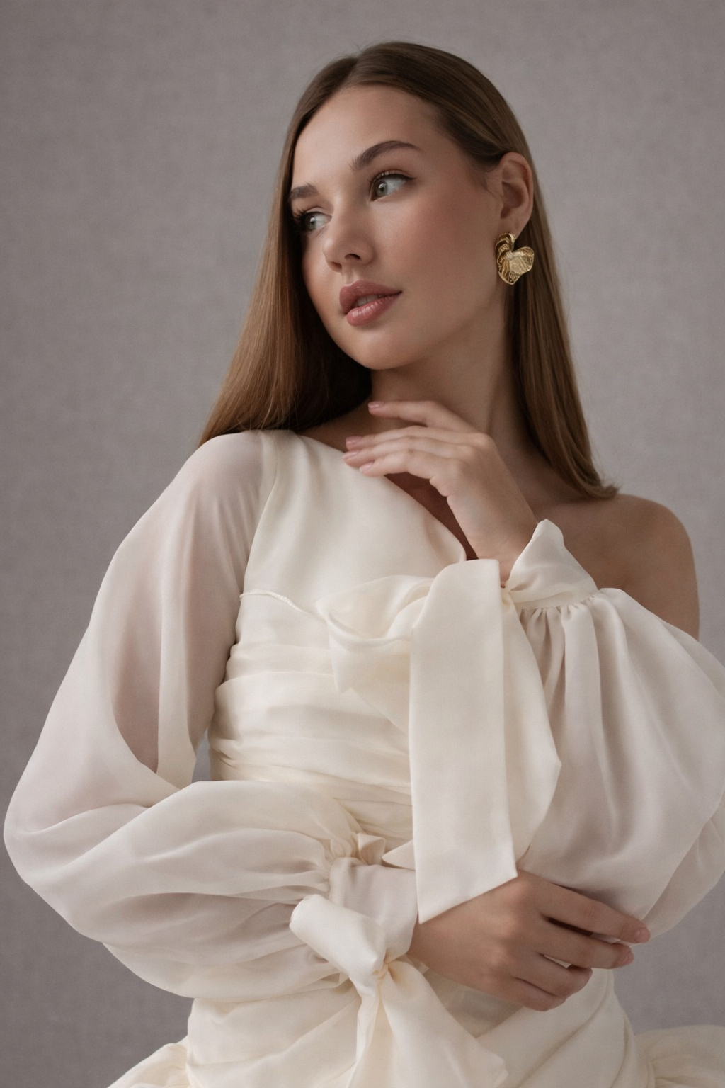 Woman wearing a white off-shoulder dress with long sleeves against a gray background