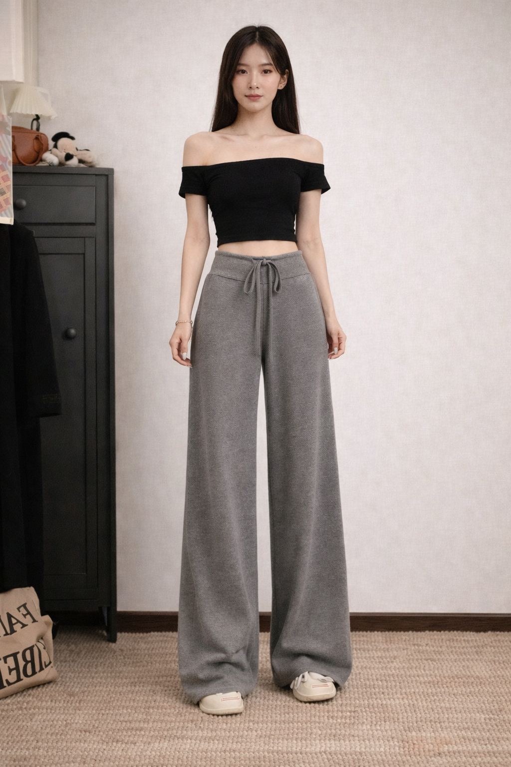 Woman wearing a black off-shoulder top and gray wide-leg pants in a room.