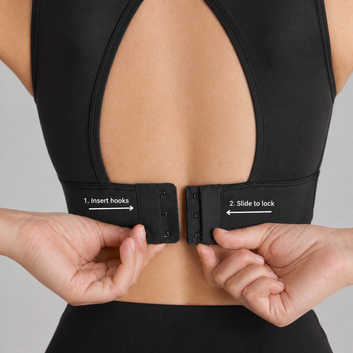 Black sports bra with hook and eye closure being adjusted on a person against a gray background
